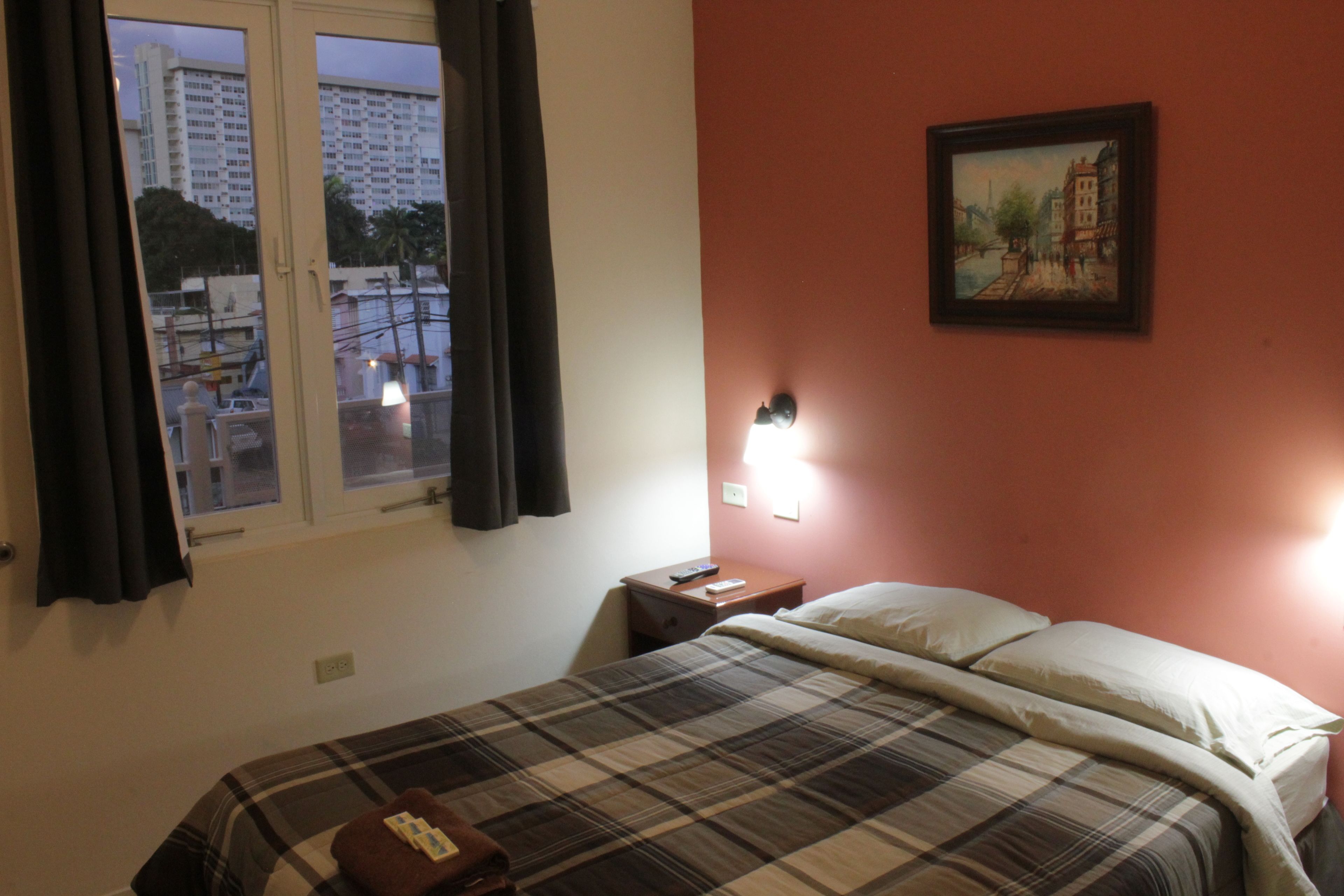 Une chambre d’hôtel avec un lit, une table de chevet, un tableau au mur et une fenêtre avec des rideaux.