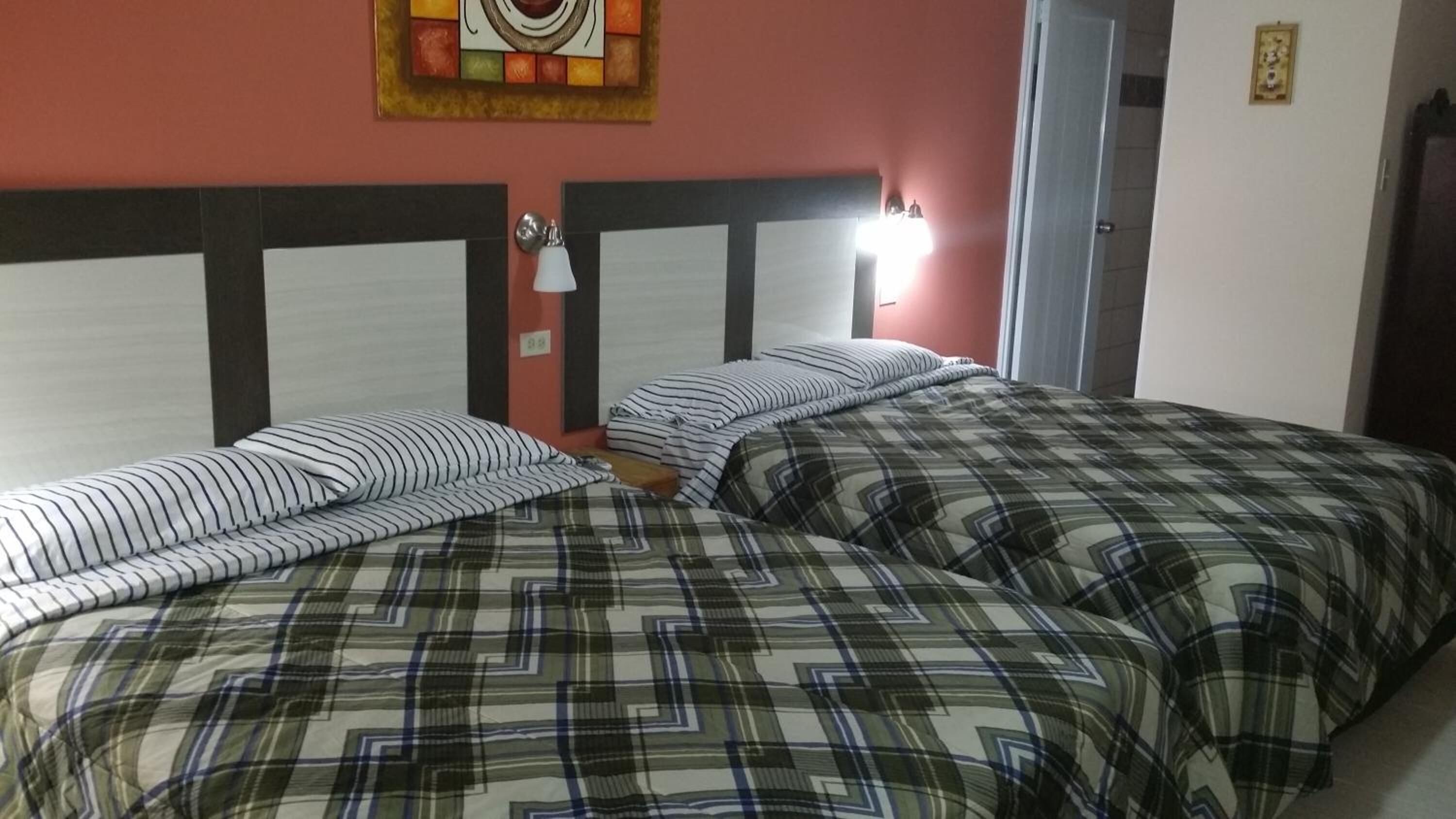 Una habitación con dos camas, cada una con ropa de cama a rayas y cuadros. Hay un reloj de pared y un cuadro enmarcados sobre las camas.