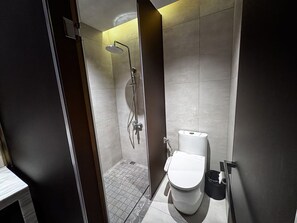 A modern bathroom with a shower, toilet, and a small trash bin.