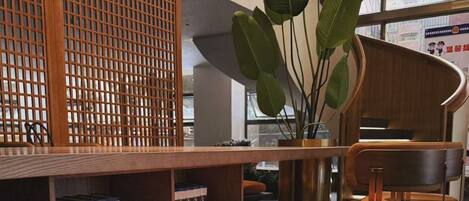 A reception area with a wooden desk, a bench, a large plant, and a bookshelf with books.