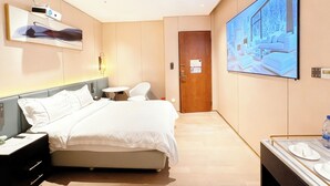 Een hotelkamer met een bed, nachtkastjes, een televisie, een klein tafeltje met stoelen, en een deur.