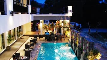 A swimming pool with a water fountain feature, surrounded by outdoor seating and tables.