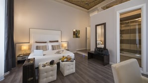 A hotel room with a large bed, a desk with a laptop, a suitcase, and a bathroom with a shower. - Arenula Suites (Rome)