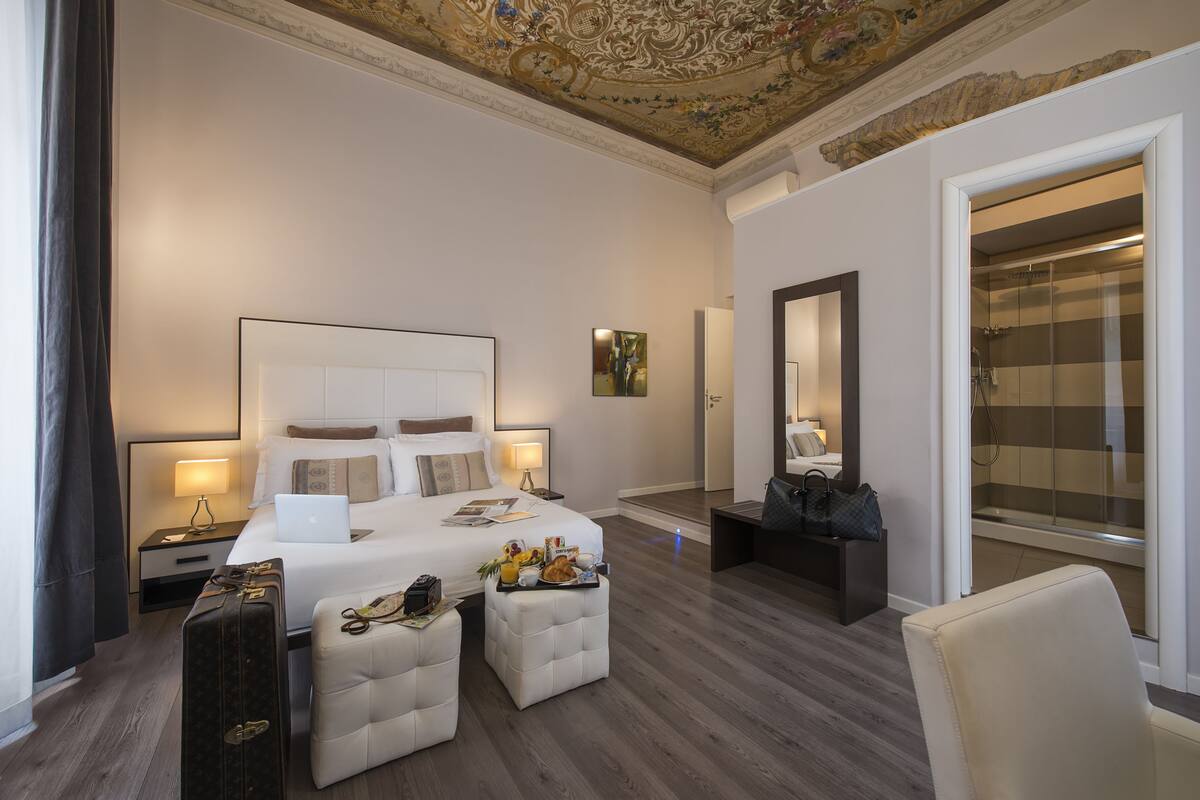 Une chambre d’hôtel avec un grand lit, un bureau avec un ordinateur portable, une valise et une salle de bain avec douche.