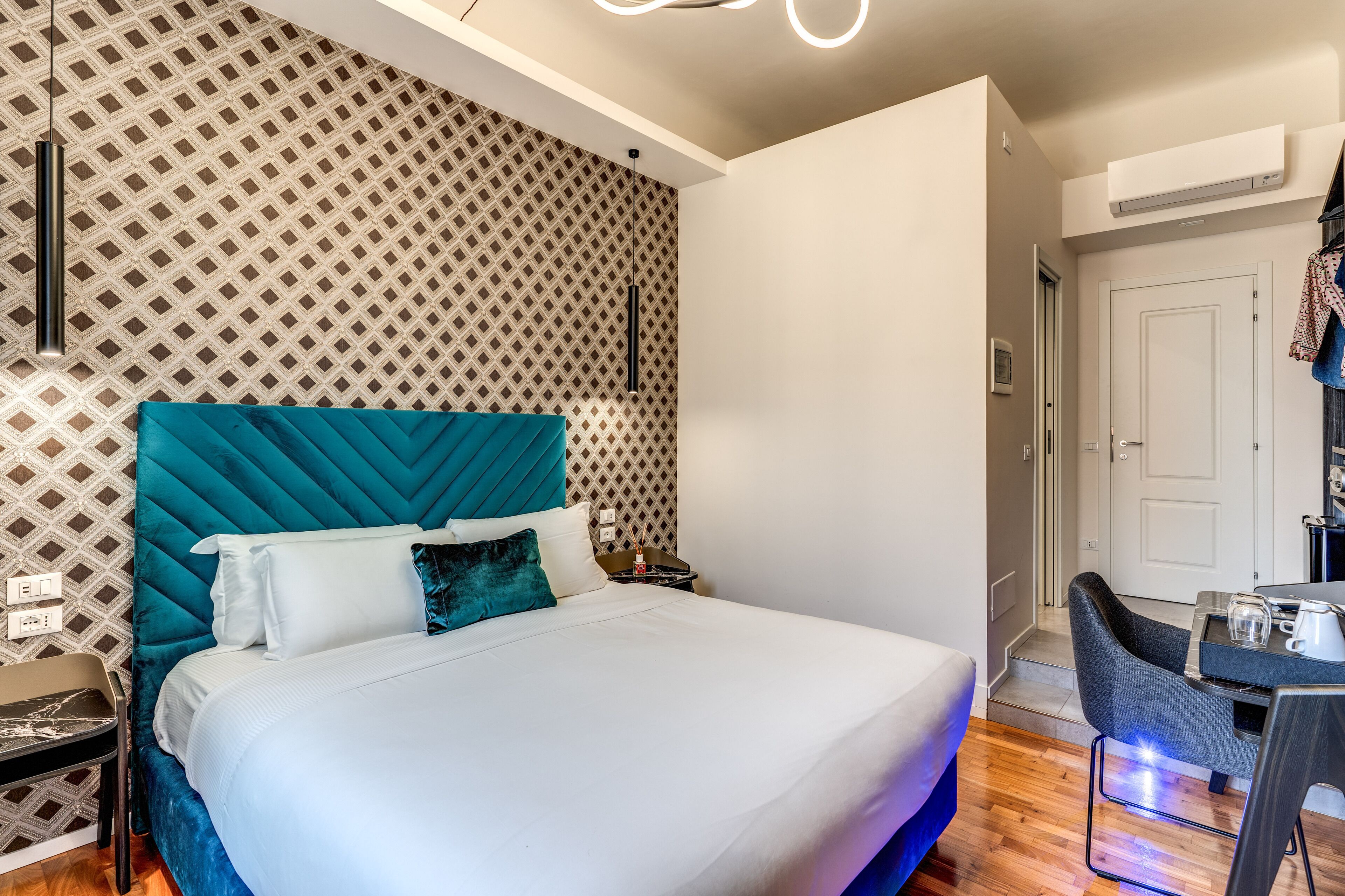 A modern hotel room with a large bed, a desk, and a patterned wall.