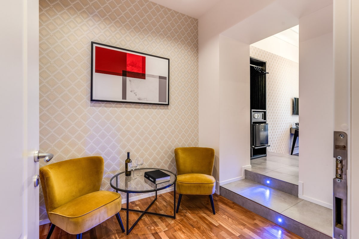 Un salon moderne avec deux fauteuils jaunes, une table basse en verre et une œuvre d’art abstraite encadrée accrochée au mur.