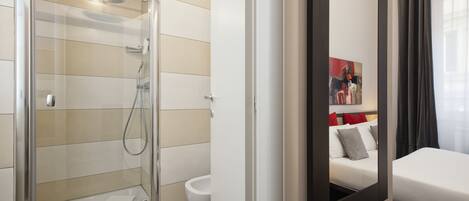 A modern bathroom with a glass-enclosed shower, a toilet, and a bed with a mirror reflecting a painting and a nightstand.