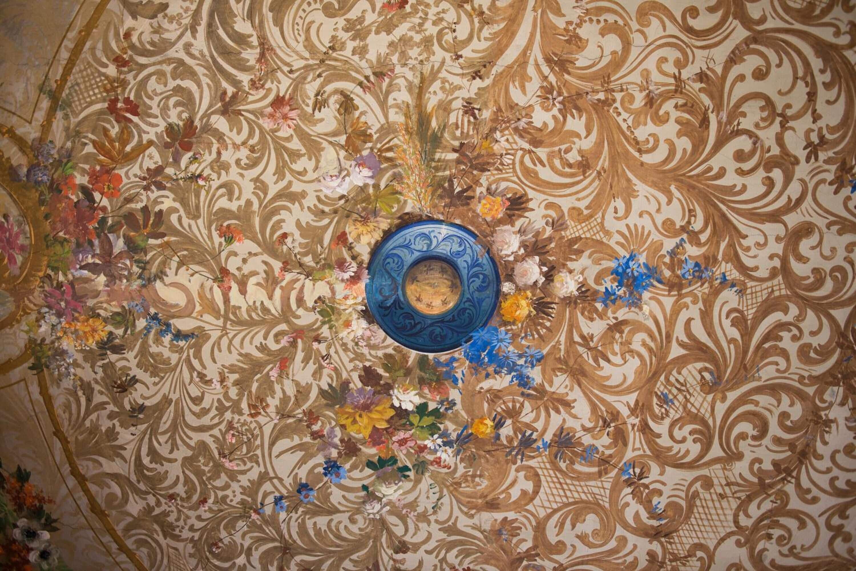 Un plafond orné d’un motif floral et d’une plaque bleue au centre.