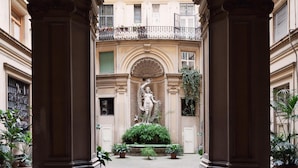 A courtyard with a statue, columns, and potted plants. - Arenula Suites (Rome)