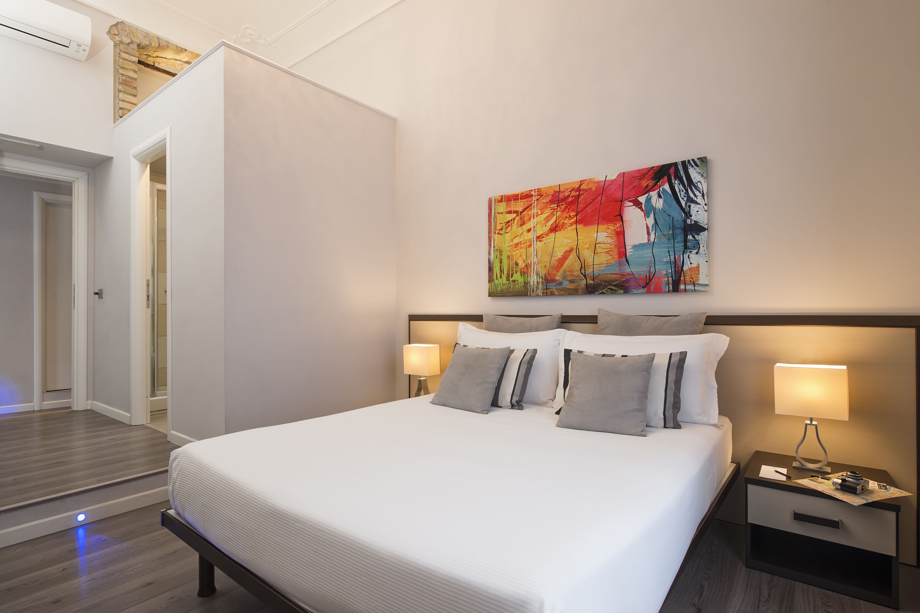 Une chambre d’hôtel moderne avec un grand lit, deux tables de chevet et un tableau abstrait aux couleurs vives accroché au mur.