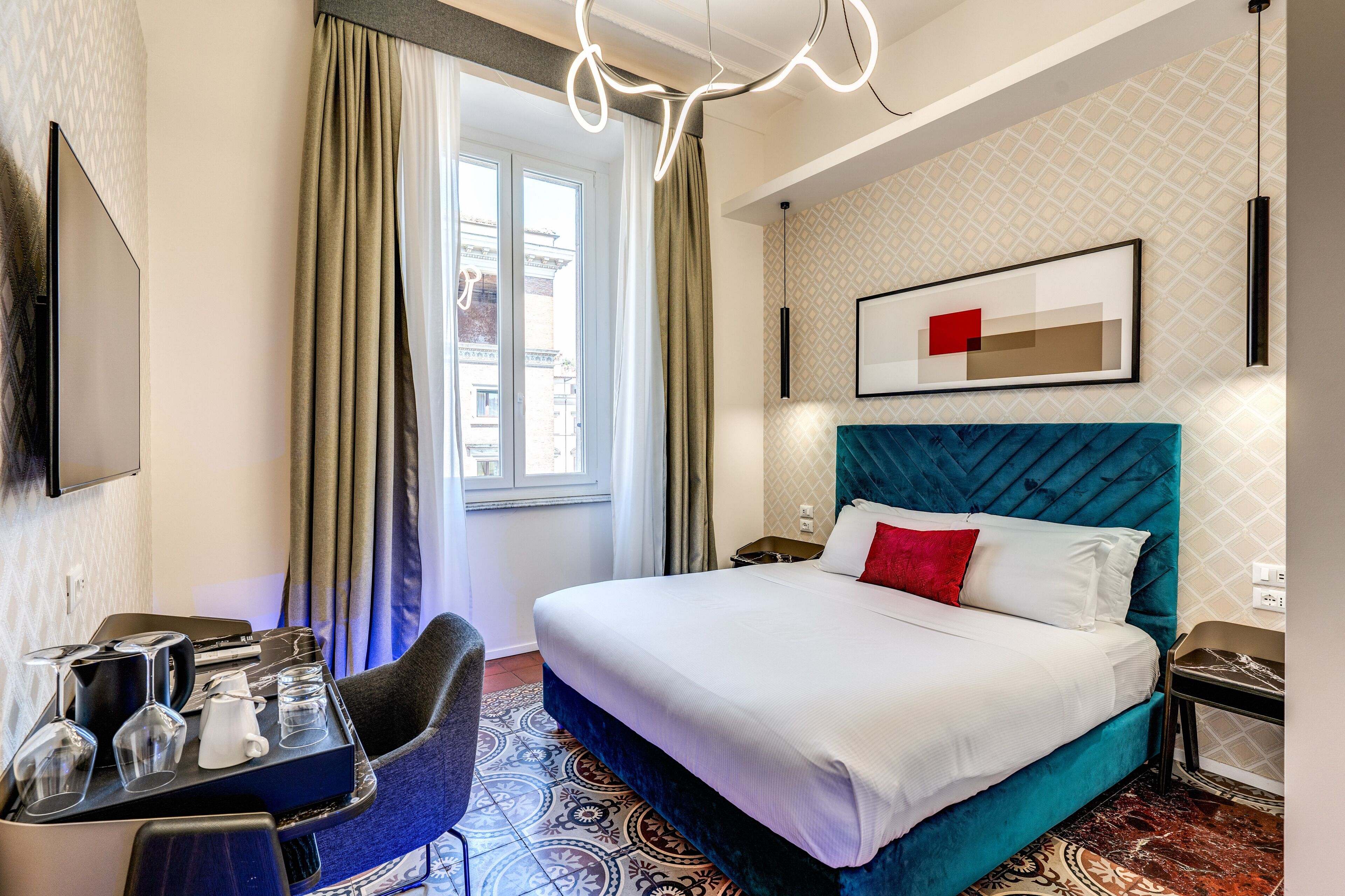 A hotel room with a bed, a desk with a chair, a TV, and a window with curtains.