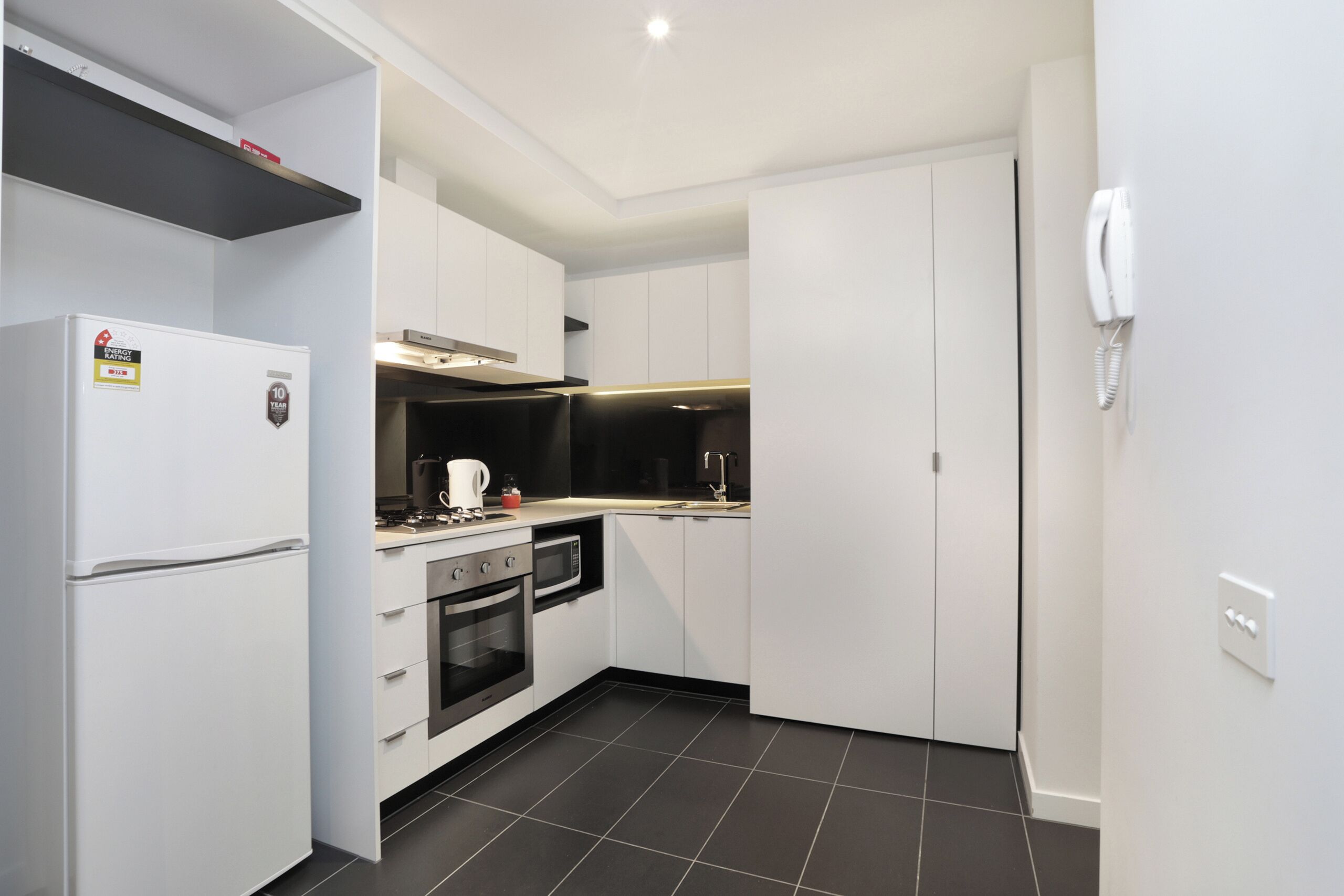 A compact kitchen with white cabinets, a built-in oven, a microwave, and a refrigerator.