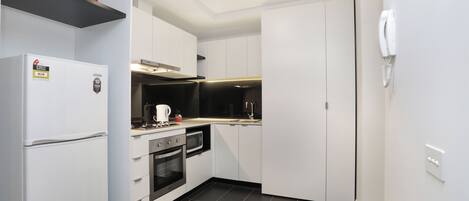 A compact kitchen with white cabinets, a built-in oven, a microwave, and a refrigerator.