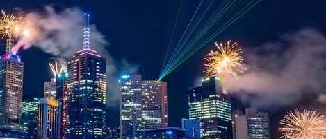 Un horizonte urbano nocturno con edificios iluminados y fuegos artificiales.