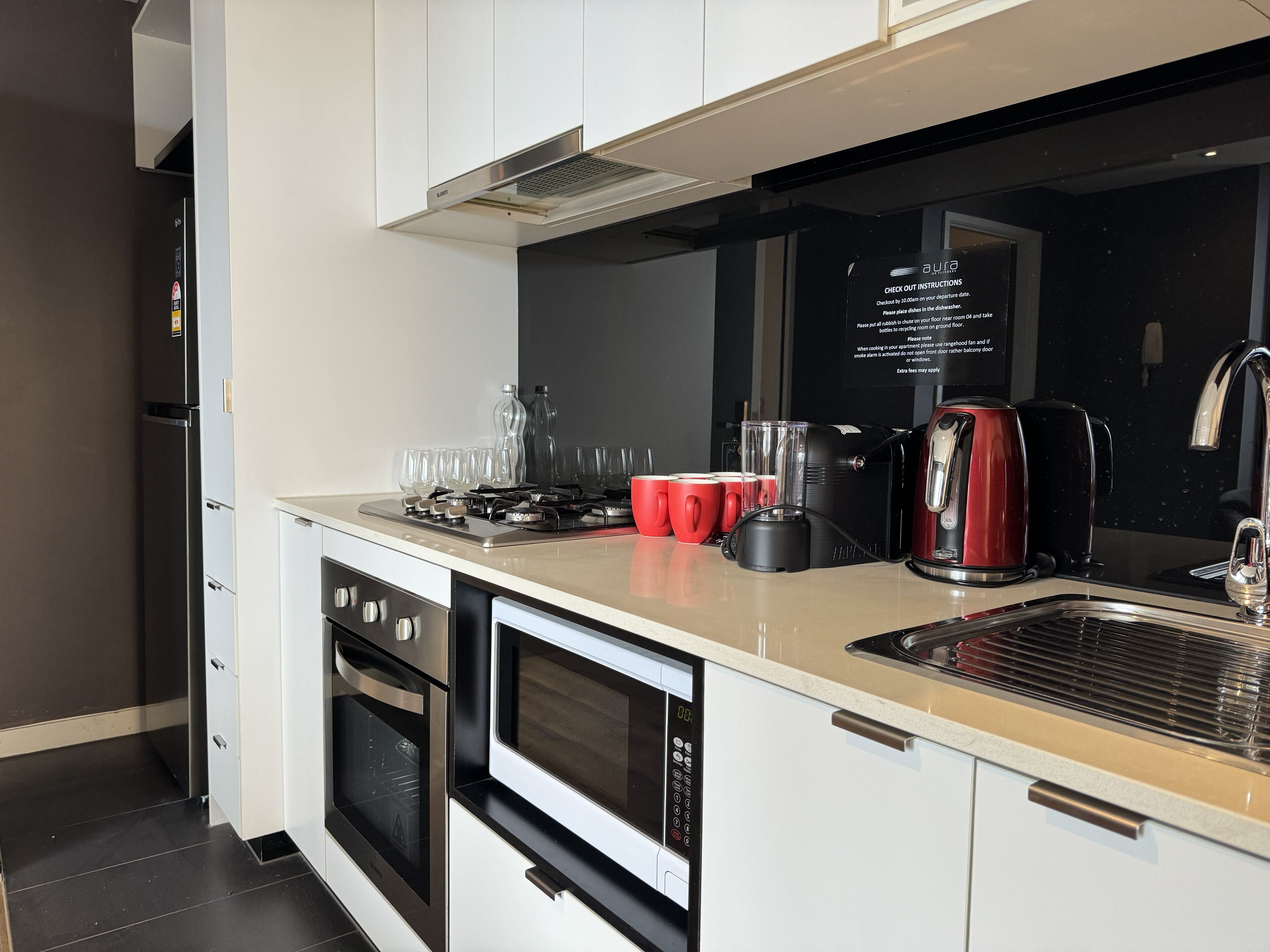 Une cuisine moderne équipée d’un four encastré, d’un four à micro-ondes et d’une cuisinière à gaz. On peut voir des tasses rouges et une machine à café sur le plan de travail.