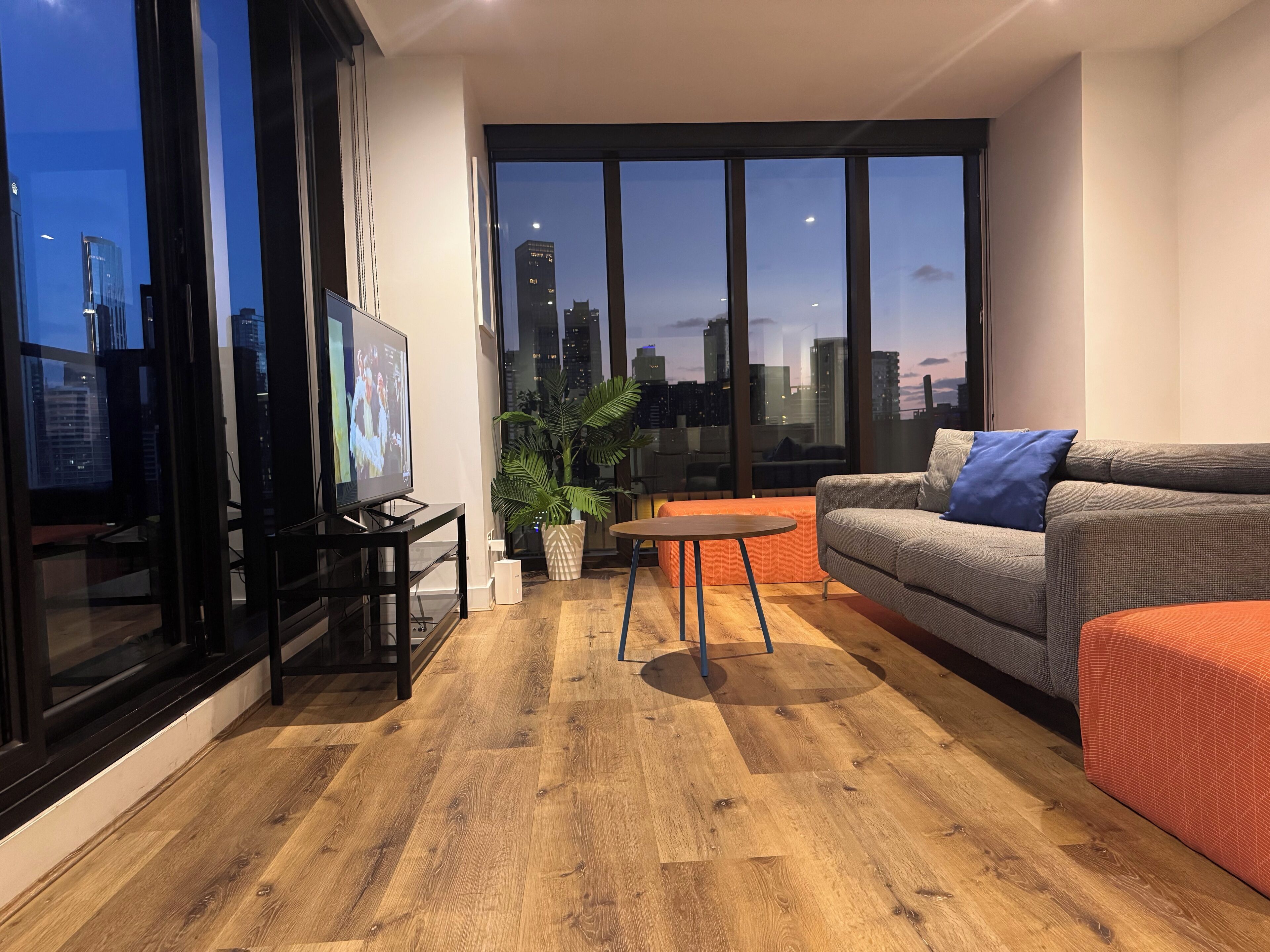 A modern living room with a large TV, a sofa, a coffee table, and a potted plant.