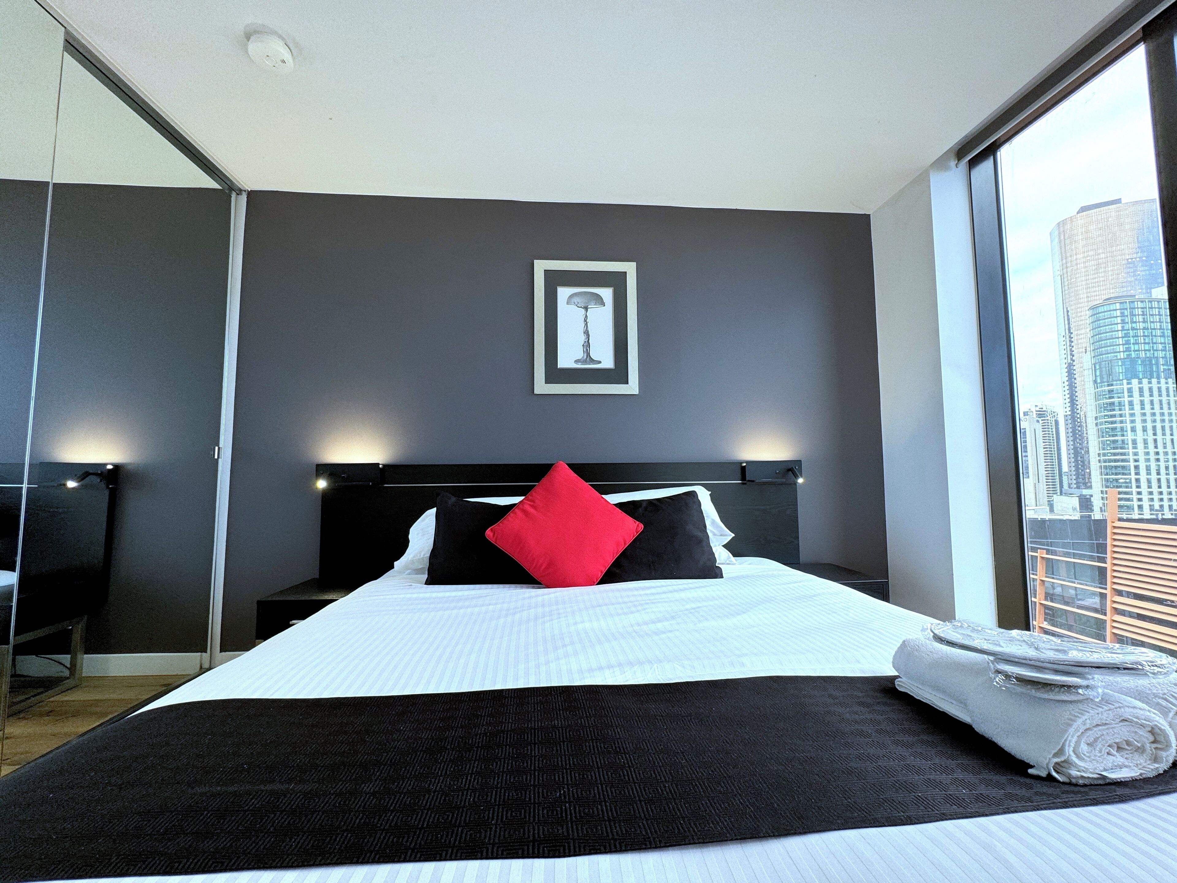 Ein modernes Hotelzimmer mit einem großen Bett, Blick auf die Stadt und einem gerahmten Bild an der Wand.