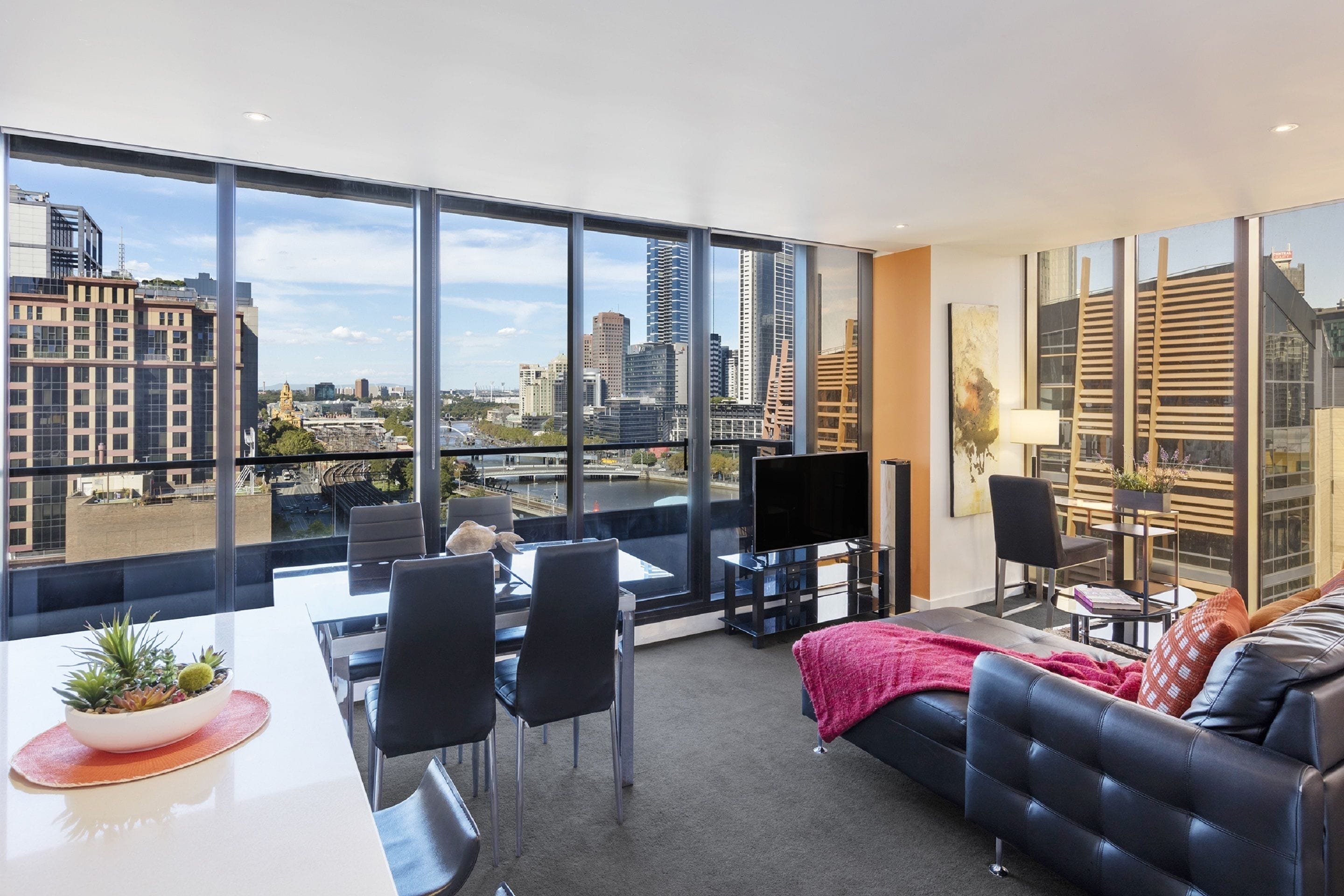 A modern living room with a large window, a sofa, a dining table, and a TV.