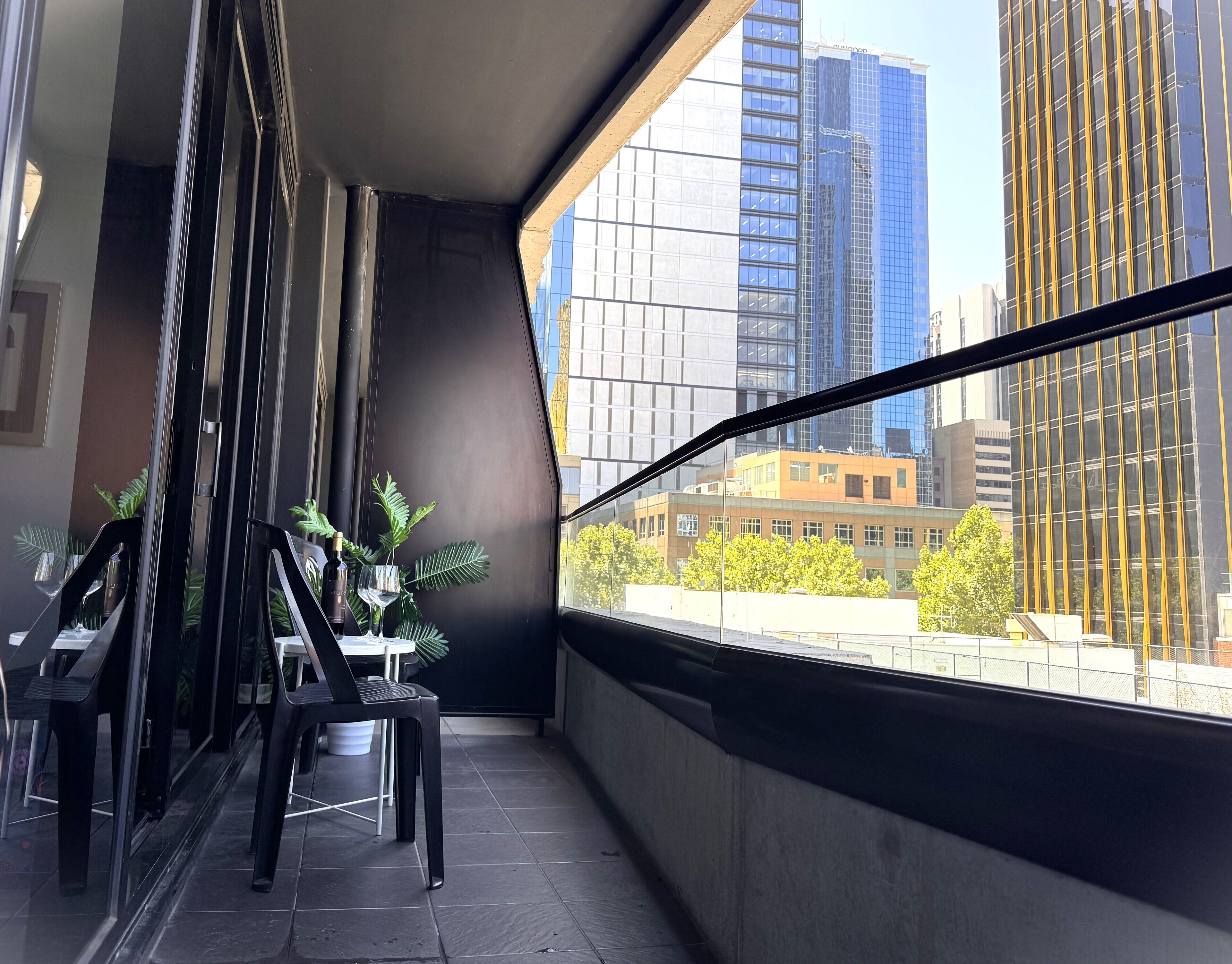 A balcony with a view of modern buildings, a table with chairs, and potted plants.