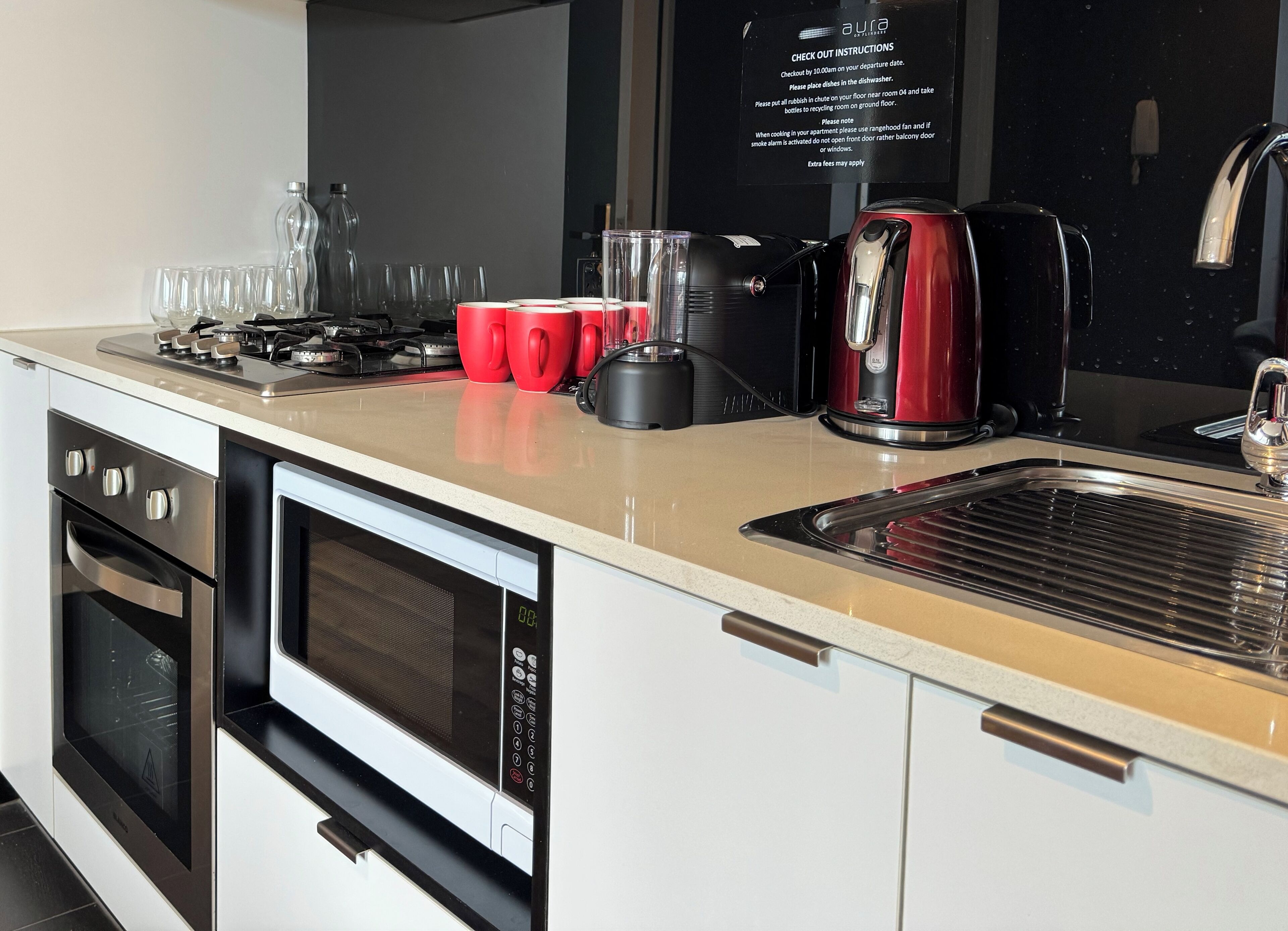 A modern kitchen with a stainless steel range hood, a red coffee maker, and a built-in oven.