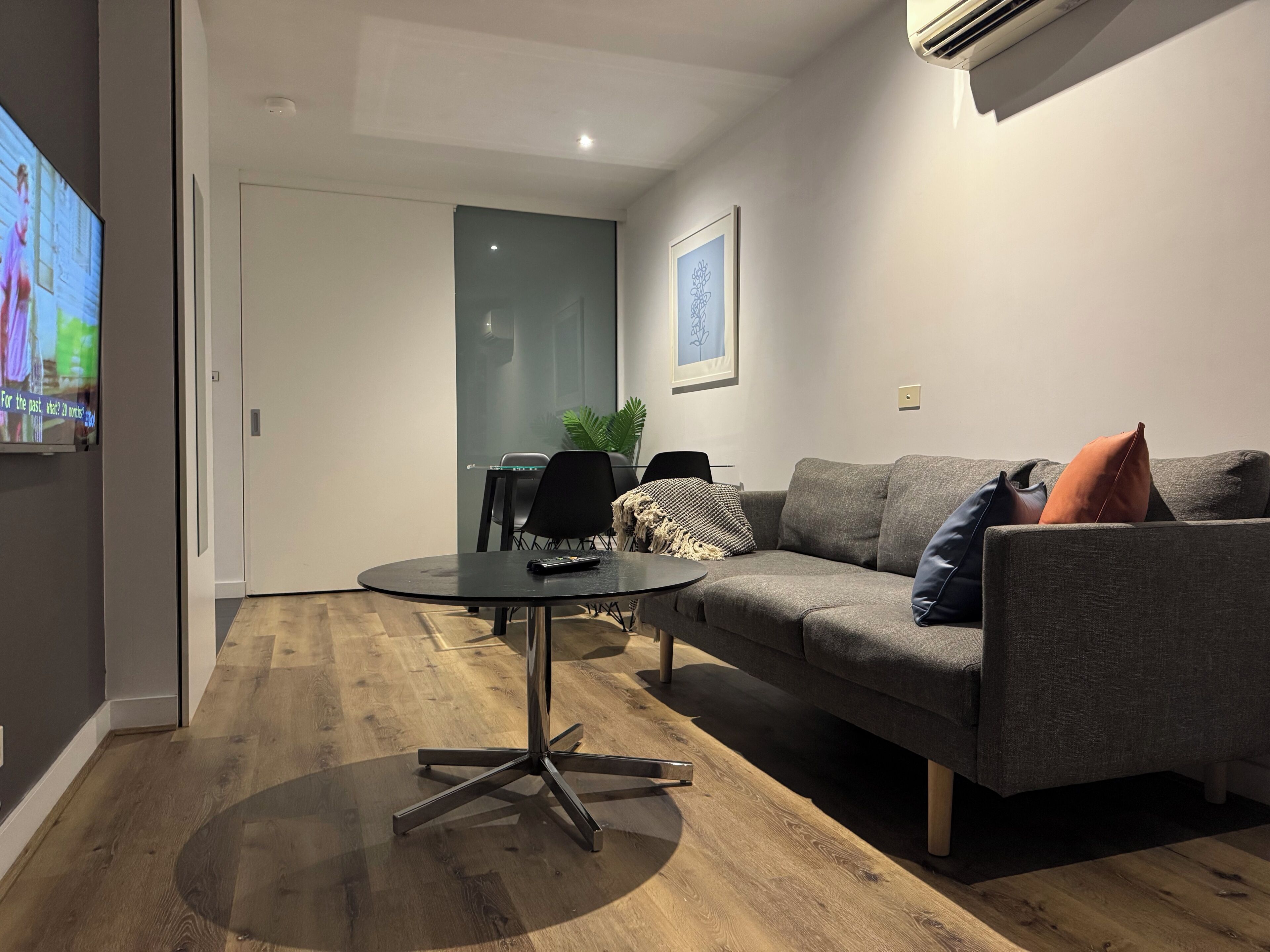 Una sala de estar moderna con un sofá gris, una mesa redonda negra y un televisor montado en la pared.