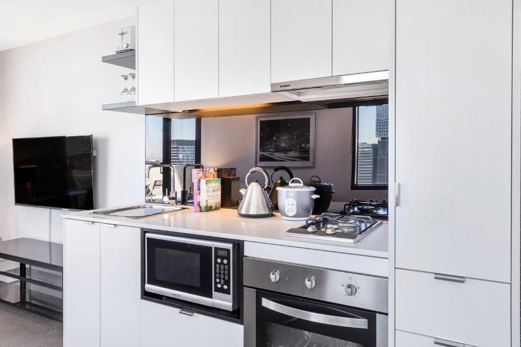 A modern kitchen with a built-in oven, microwave, and gas stove. There is a window above the stove, and a flat-screen TV mounted on the wall.