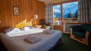 A room with a bed, a chair, a window with a mountain view, and a radiator. - Hôtel Arbois Bettex (Saint-Gervais-les-Bains)