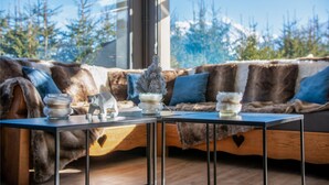A cozy seating area with a fur-covered sofa, a glass table with decorative items, and a view of trees through a window. - Hôtel Arbois Bettex (Saint-Gervais-les-Bains)