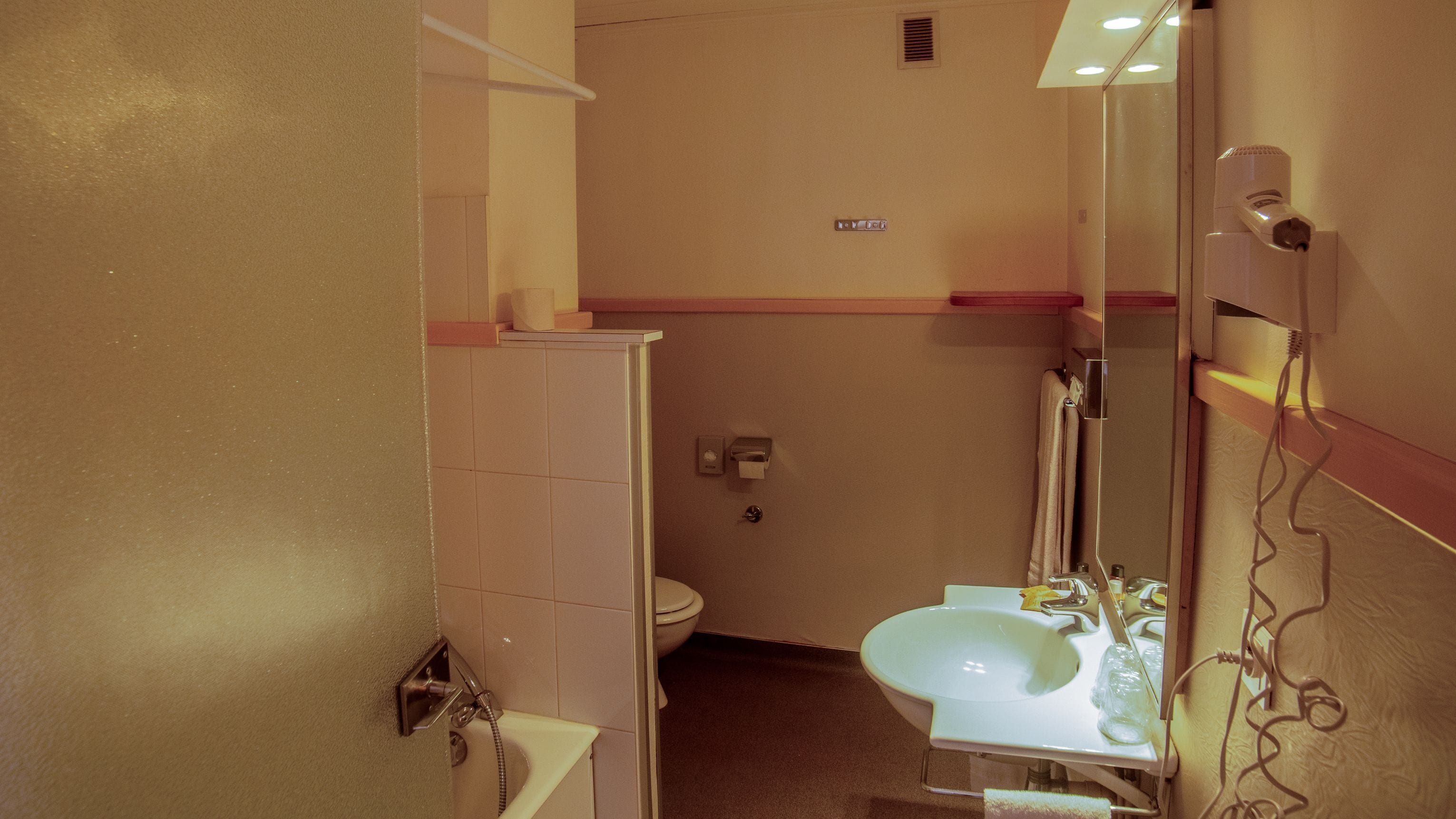 Ein kleines Badezimmer mit Toilette, Waschbecken und Dusche. Ein Handtuchhalter und ein Spiegel sind vorhanden.