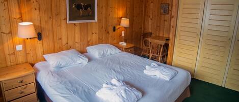 A wooden-paneled room with a large bed, two bedside lamps, a framed picture, a small table, and a chair.