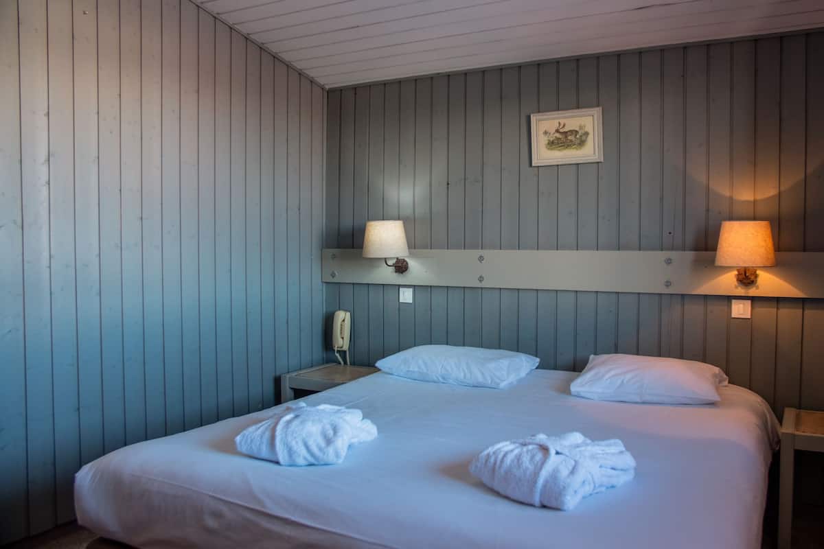 A hotel room with a bed, two bedside lamps, a telephone, and a framed picture on the wall.