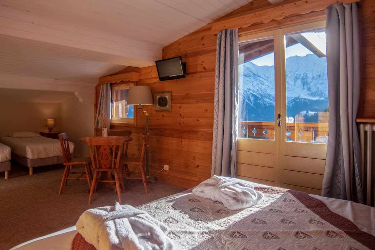 A cozy room with a bed, two single beds, a wooden table, and a TV.