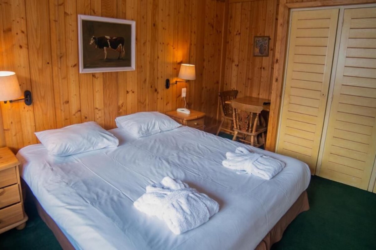 A wooden-paneled room with a large bed, two bedside tables, a chair, and a wardrobe.