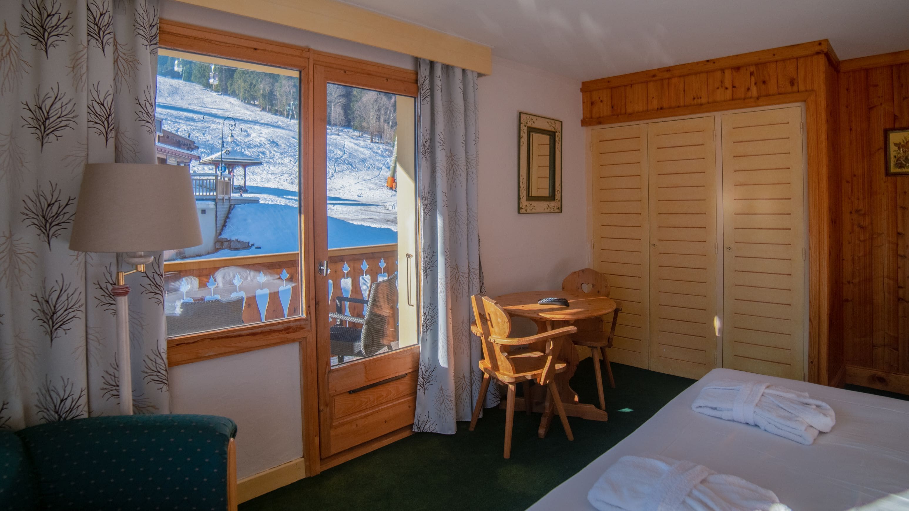 Ein Hotelzimmer mit Bett, Schreibtisch, Stuhl, Fenster mit Blick auf eine verschneite Landschaft und Holzwänden.