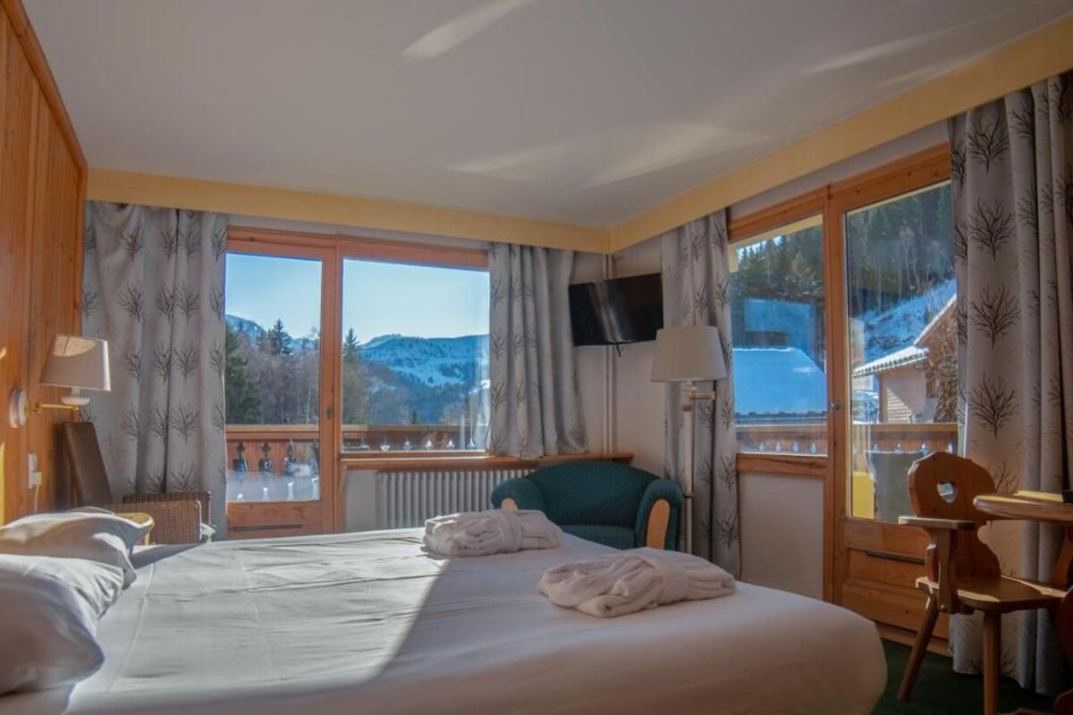 Habitación de hotel con cama, dos sillas, televisor y ventana con vista a la montaña.