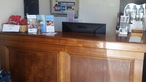 A hotel reception desk with a wooden panel design, a computer, and various items like snacks and a water dispenser. - Best Western Colonial Village Motel (Warrnambool)