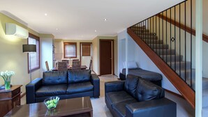 A living room with a black leather sofa, a coffee table, and a staircase with wooden railings. - Best Western Colonial Village Motel (Warrnambool)