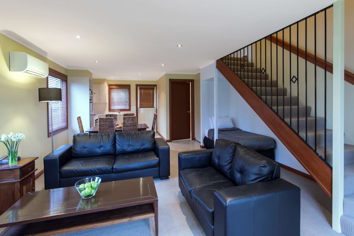 A living room with a black leather sofa, a coffee table, and a staircase with wooden railings.
