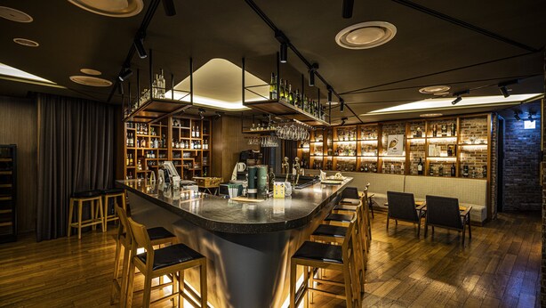 A bar area with a central bar, wooden chairs, shelves with bottles, and a brick wall. - Holiday Inn Incheon Songdo by IHG (Incheon)