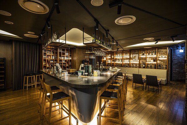 A bar area with a central bar, wooden chairs, shelves with bottles, and a brick wall. - Holiday Inn Incheon Songdo by IHG (Incheon)