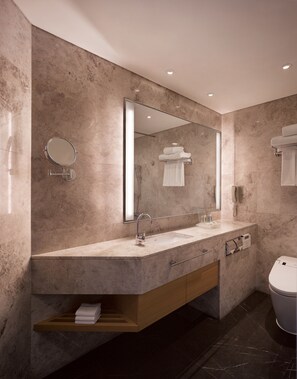 A modern bathroom with a large mirror, a sink with a towel rack, a wooden shelf, and a toilet.