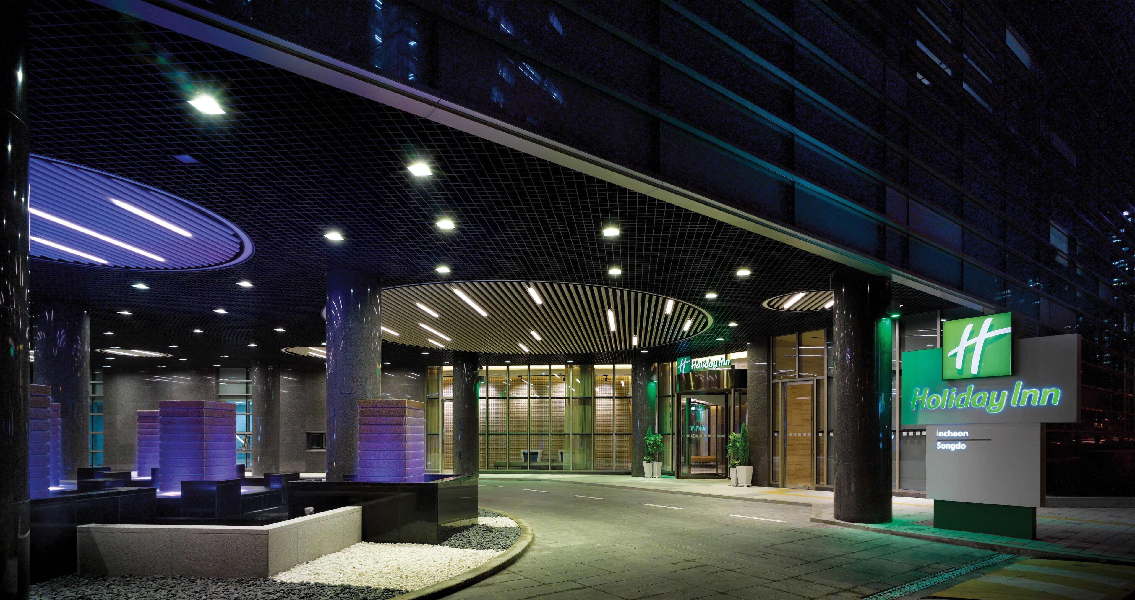 Holiday Inn -hotellin sisäänkäynti, jossa on moderni muotoilu, katettu käytävä ja selkeästi näkyvä vihreä opastekyltti.