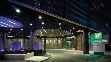 Holiday Inn -hotellin sisäänkäynti, jossa on moderni muotoilu, katettu käytävä ja selkeästi näkyvä vihreä opastekyltti.