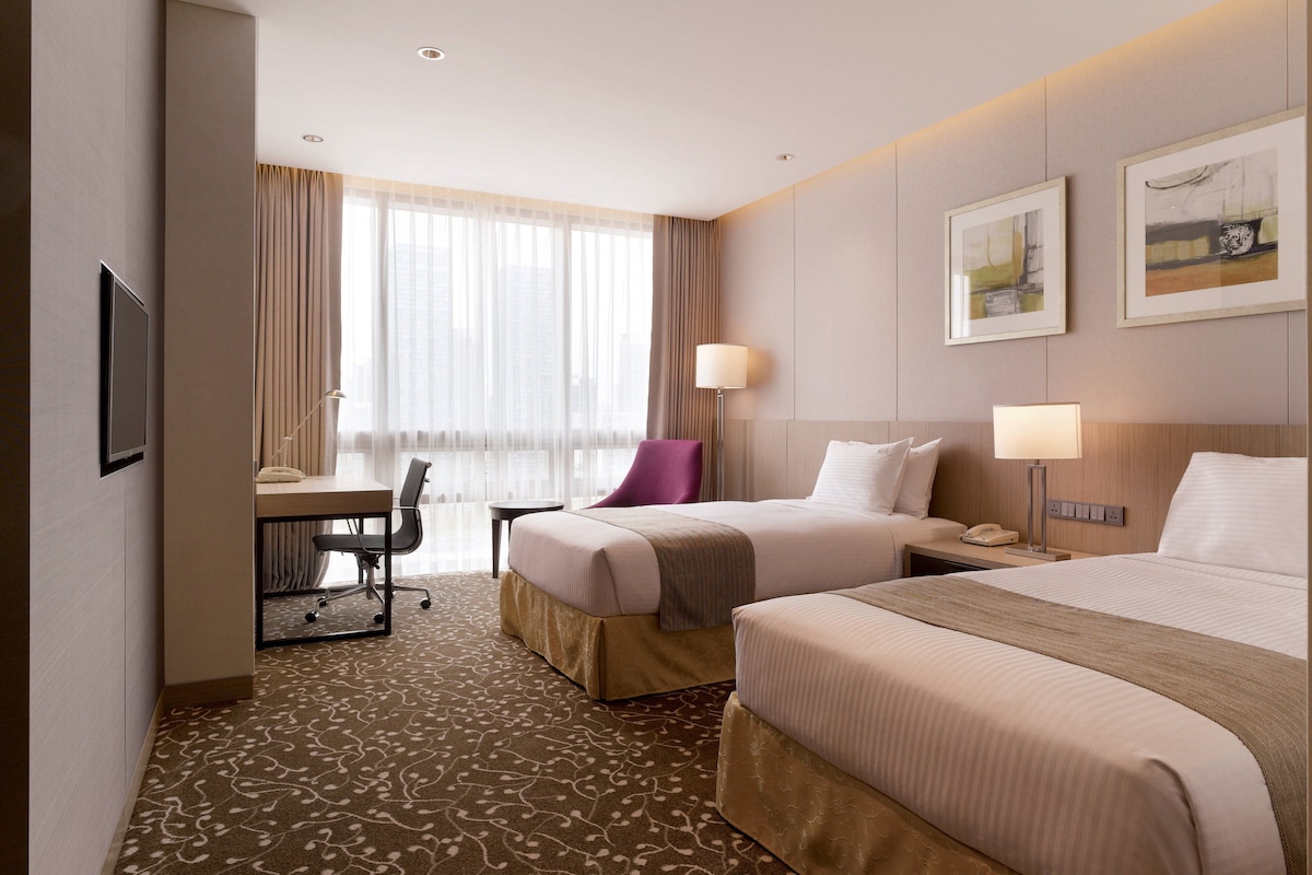 A hotel room with two beds, a desk, a chair, a lamp, and a window with curtains.