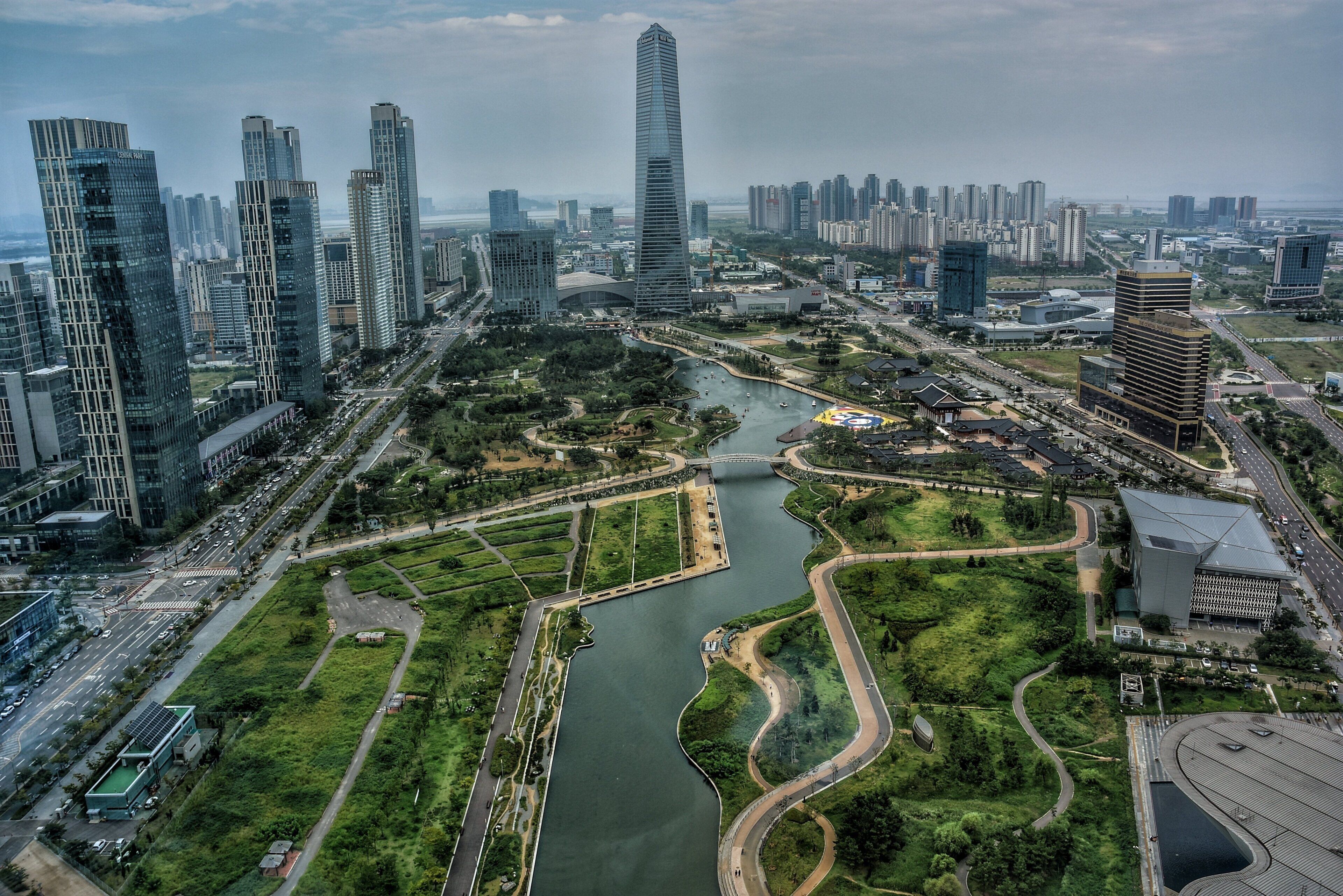 Un paisaje urbano con modernos rascacielos, un río con un puente y zonas verdes.