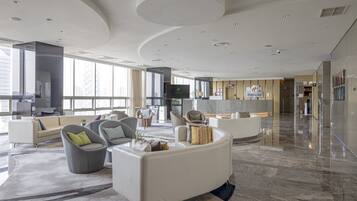 A spacious hotel lobby with modern furniture, large windows, and a central seating area.
