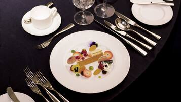 A table set with white plates, silverware, and a dessert with fruit and a chocolate piece.