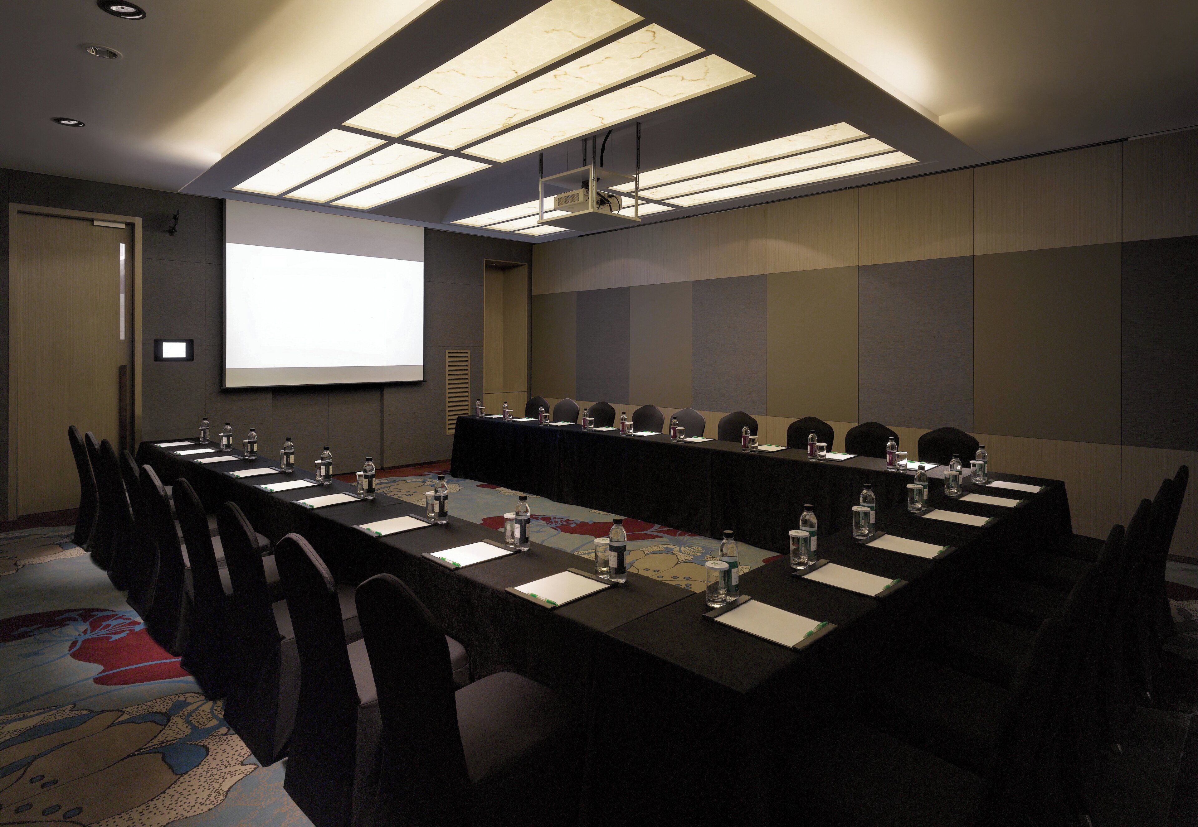 A conference room with a long table, chairs, and a projector screen.