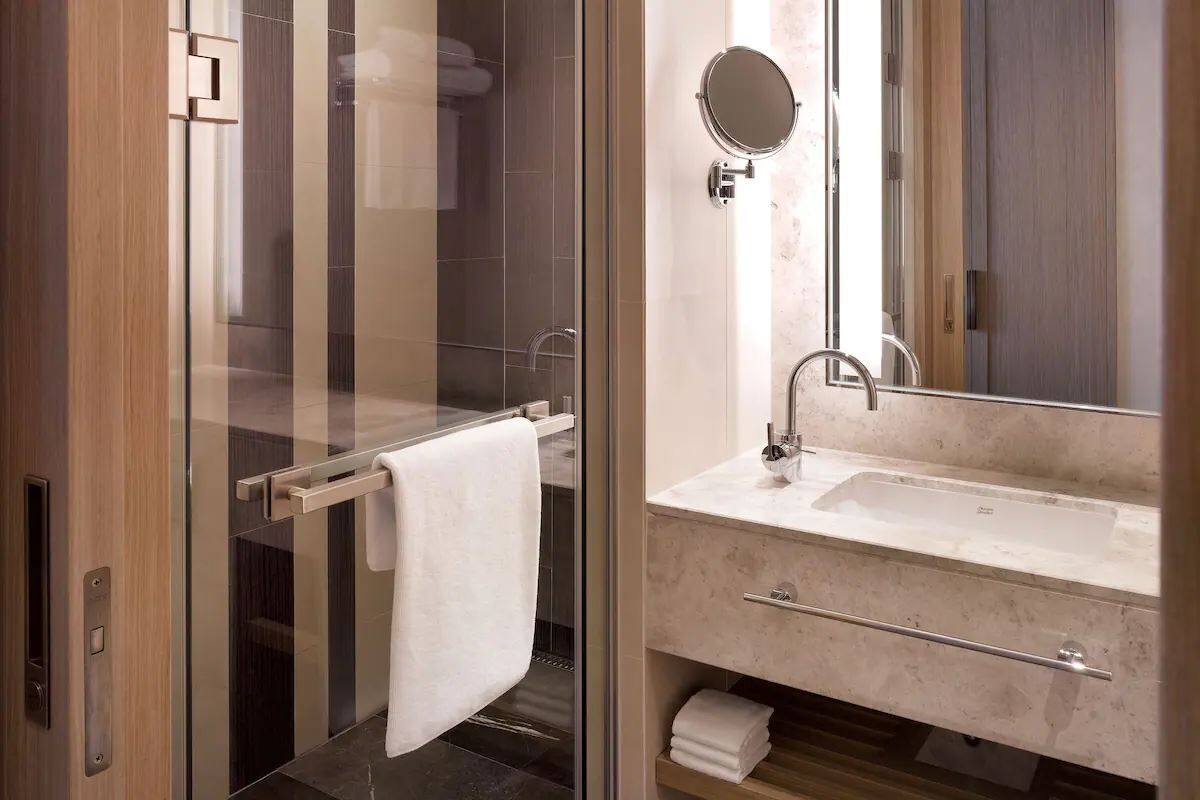 Ein modernes Badezimmer mit Duschkabine aus Glas, einem weißen Waschbecken mit Marmorplatte und einem großen Spiegel.