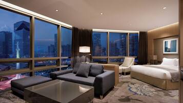 A hotel room with a large window, a sofa, a bed, a desk, and a carpeted floor.